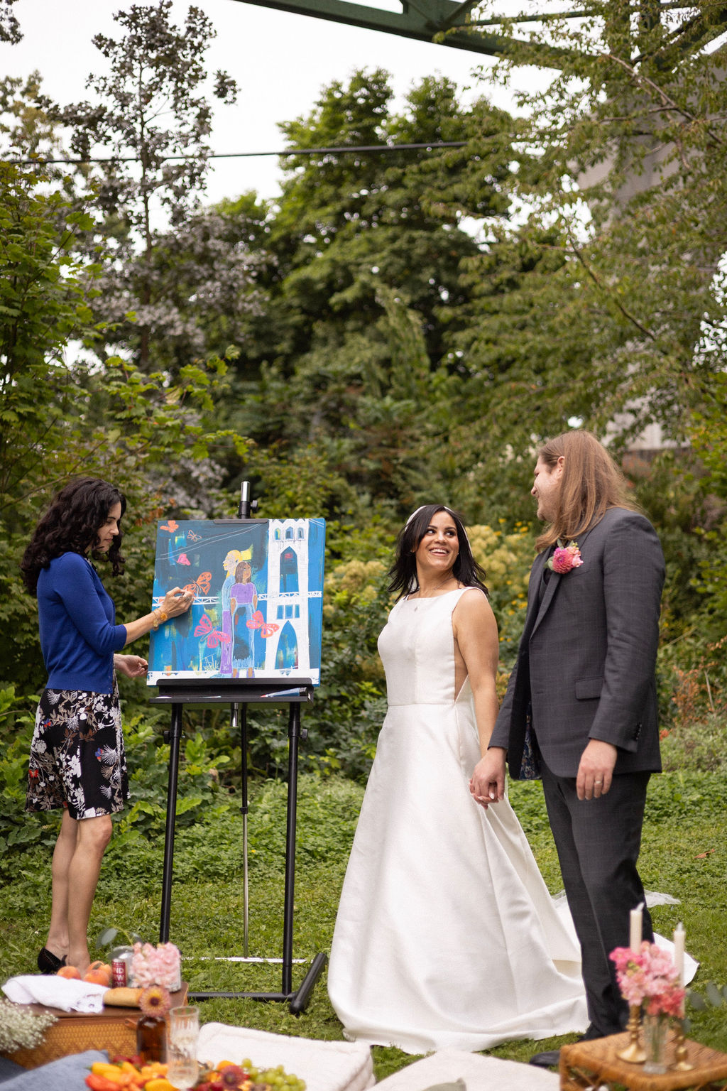A couple watching an artist paint their wedding at an easel during a Cathedral Park picnic reception