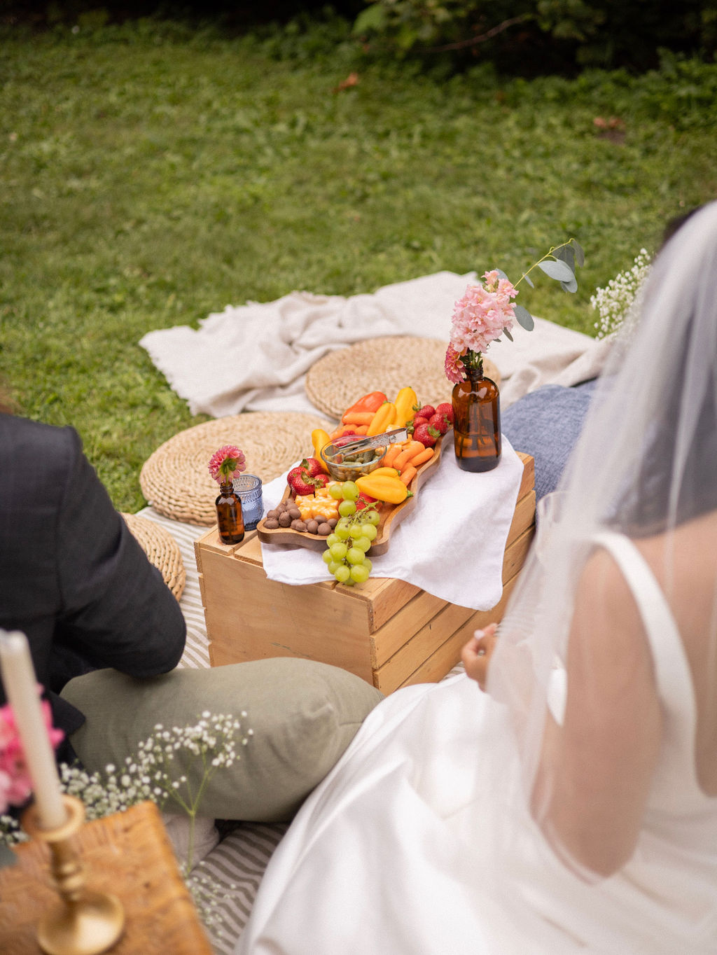 A wooden crate set with a grazing board, bud vases and blankets and cushions on the lawn