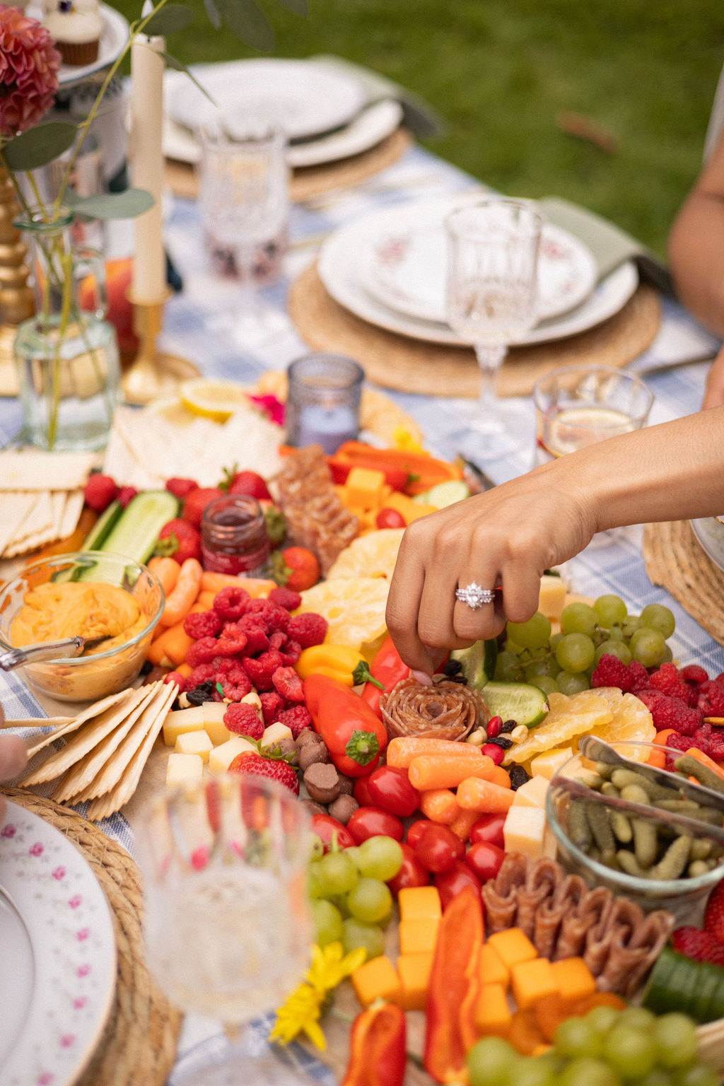 A hand reaching across a grazing spread of berries, peppers, cheese and charcuterie at a Cathedral Park picnic