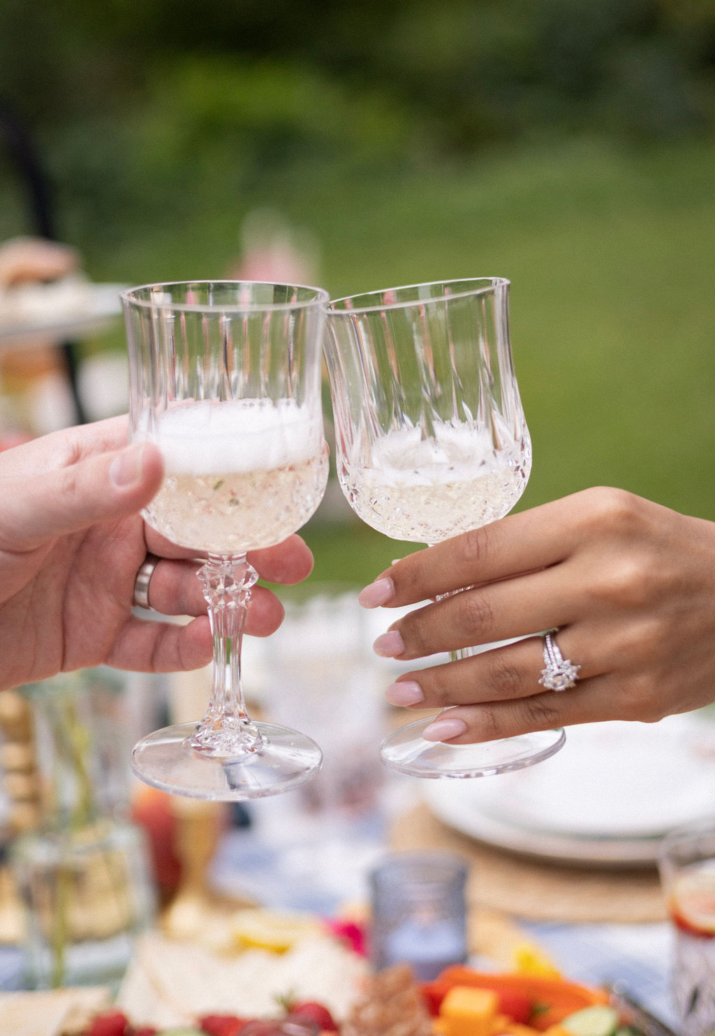 Two crystal glasses of Oregon sparkling wine touching in a toast at a Cathedral Park picnic reception