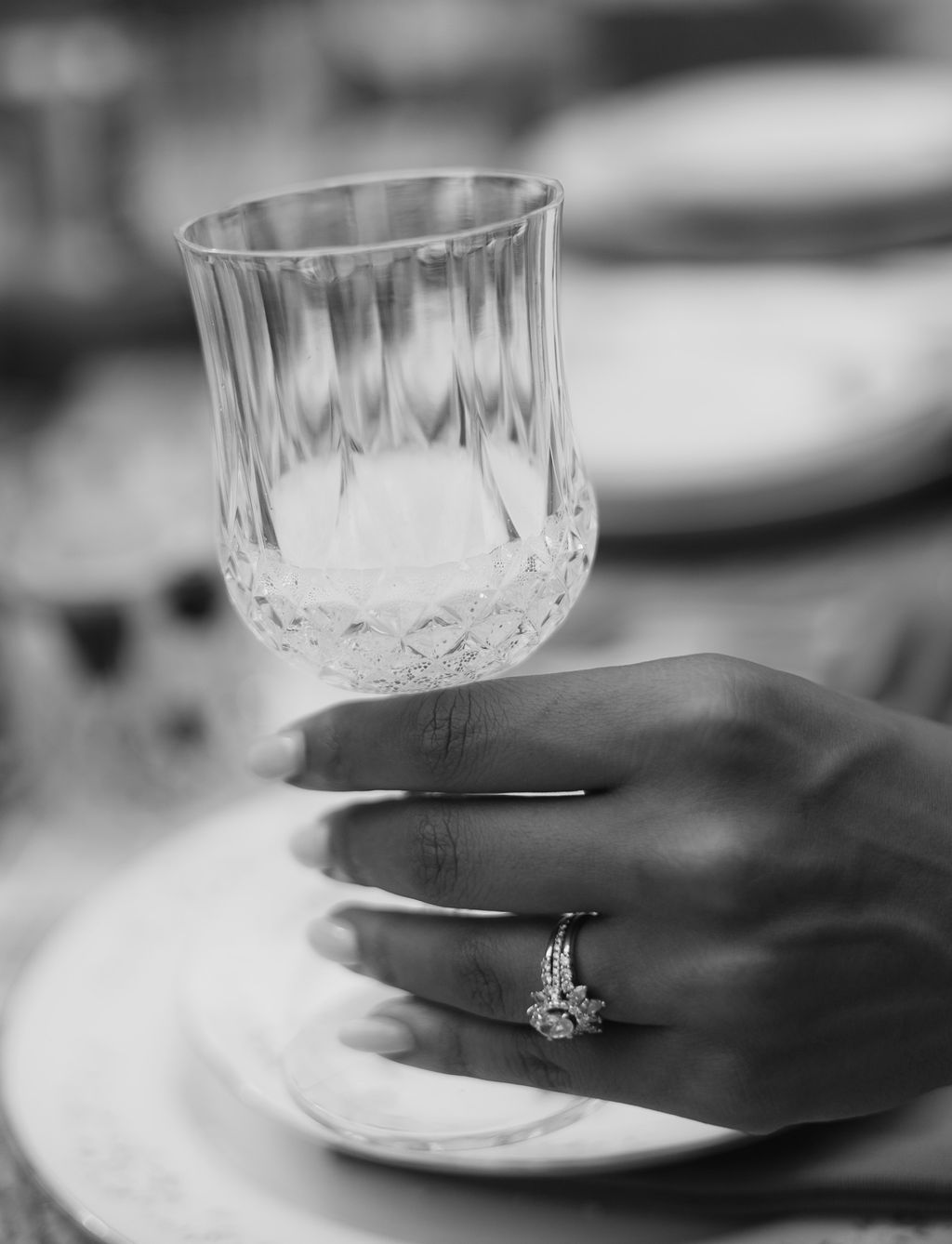 Black and white close up of a bride's hand and wedding ring holding a cut crystal glass
