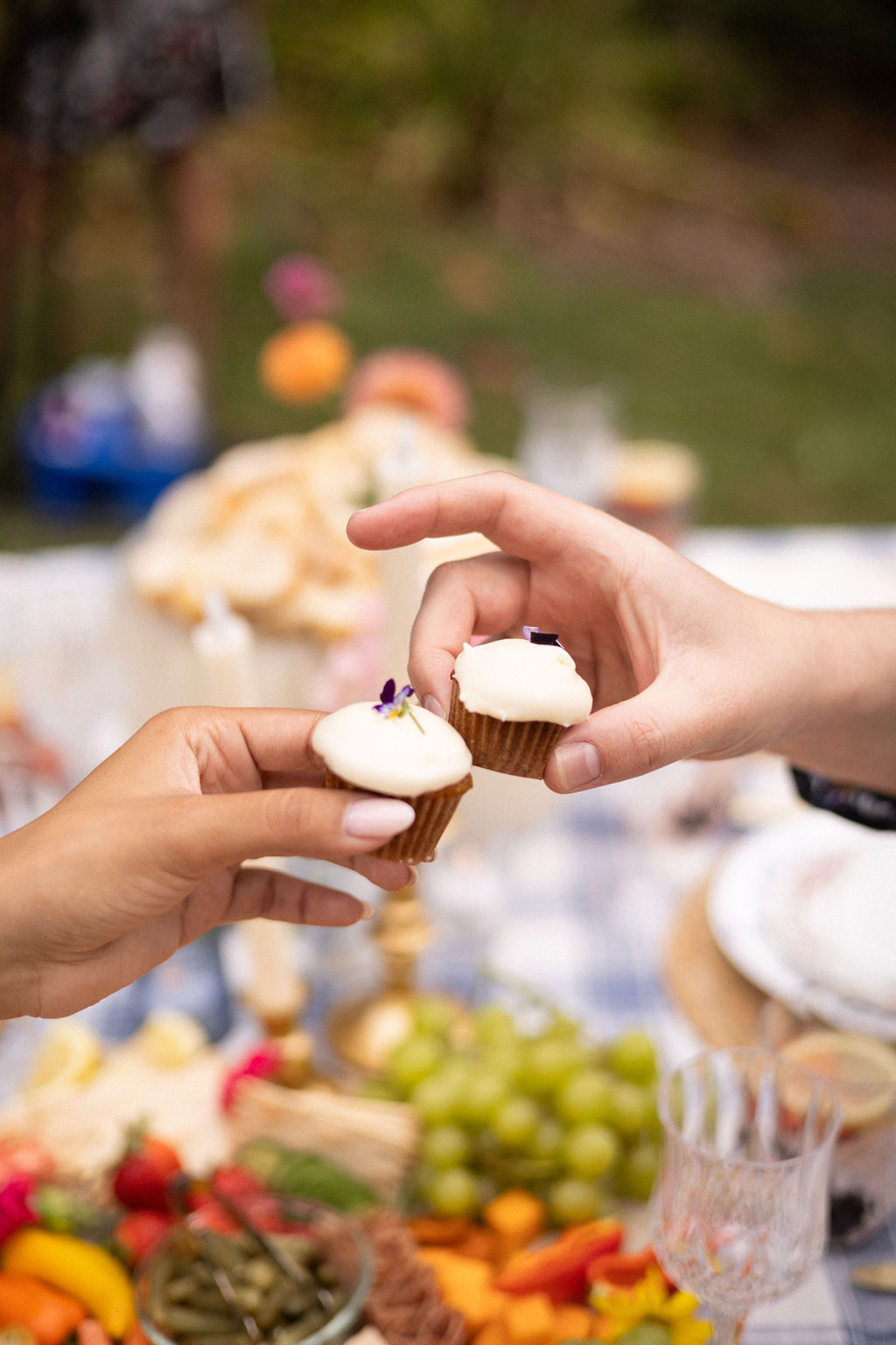 Two frosted cupcakes topped with edible flowers held over the picnic table