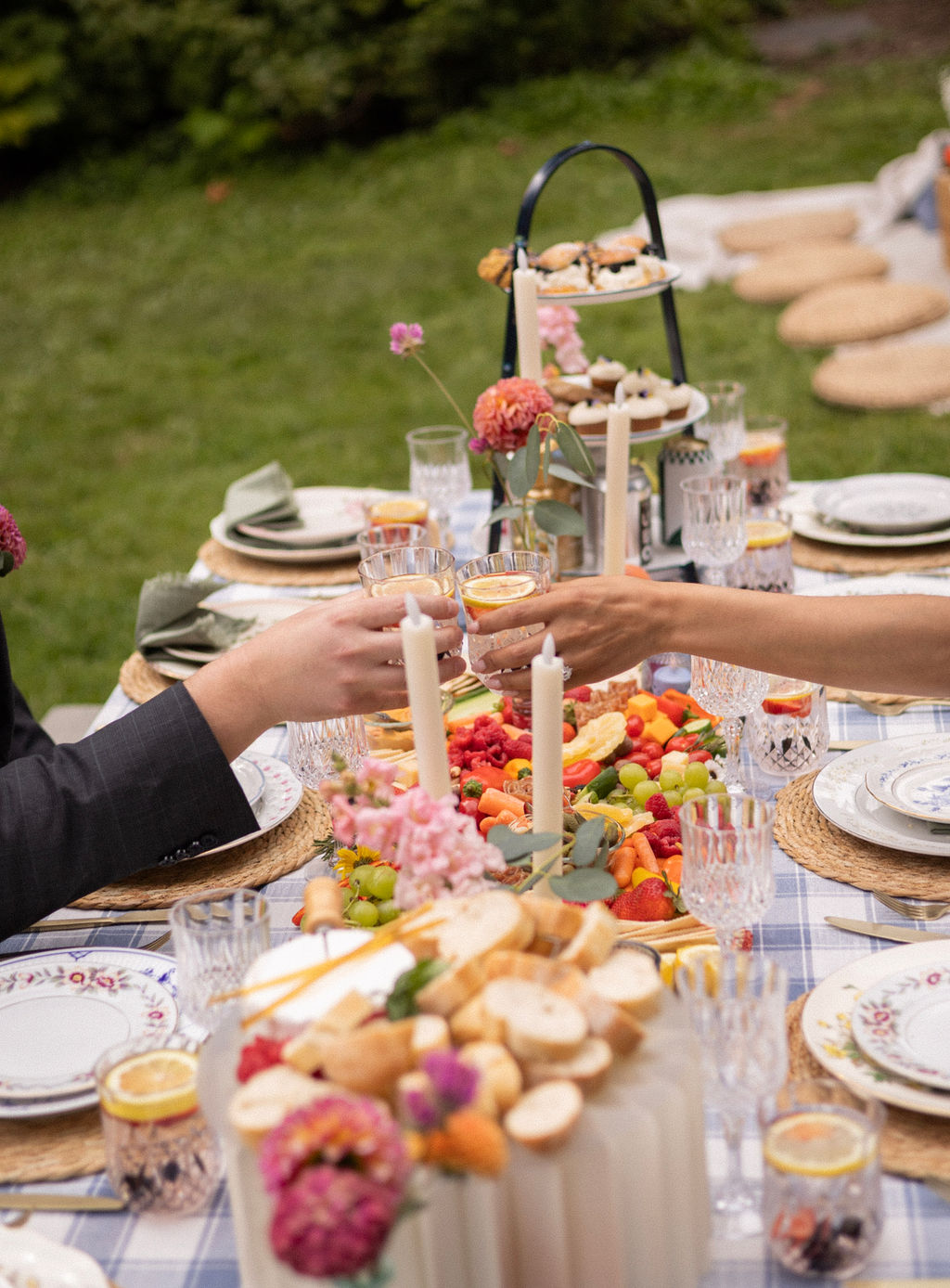 Newlyweds reaching across the picnic table to toast over the grazing spread