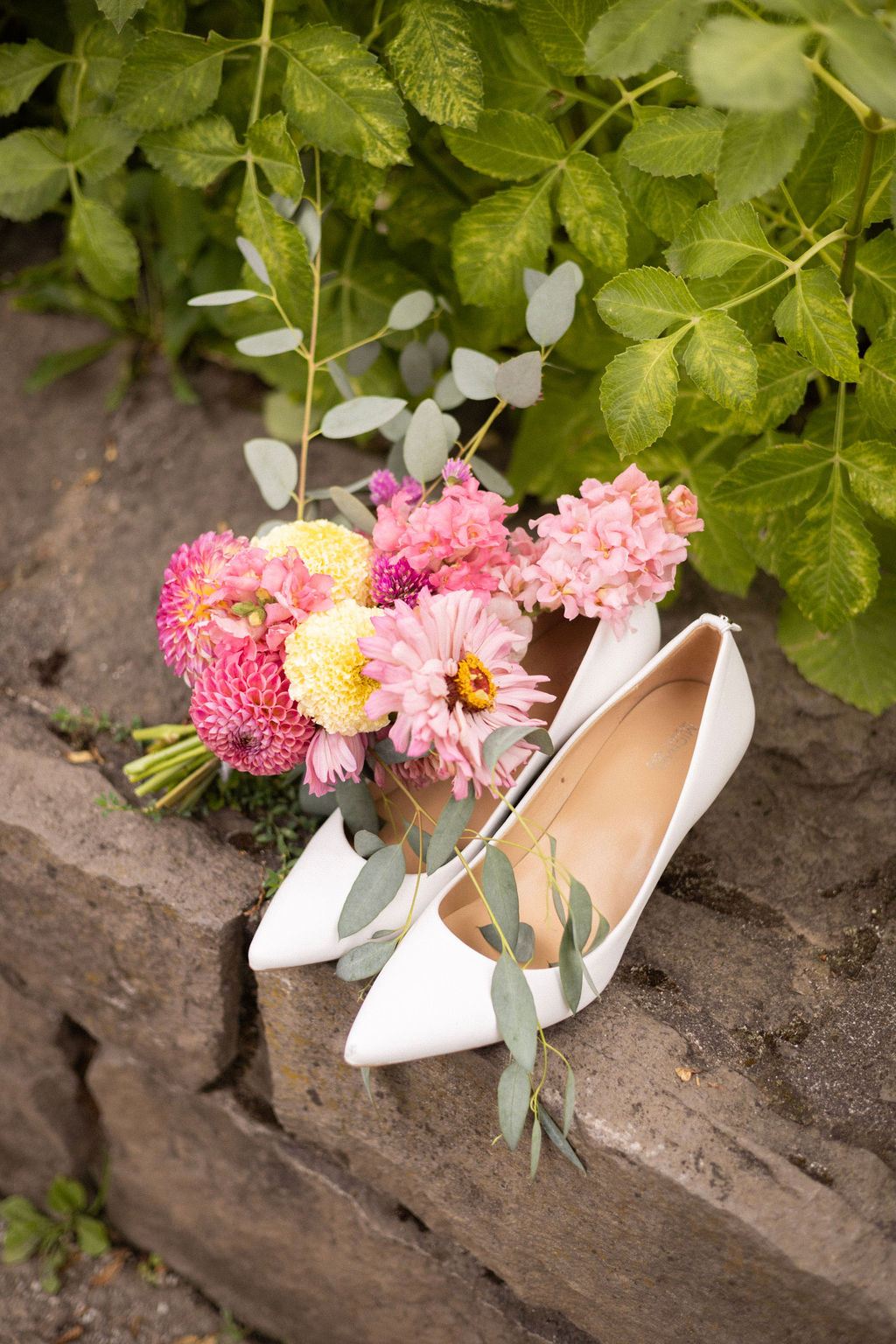 Bridal bouquet from Still City Flowers and white shoes on the stone wall at Cathedral Park