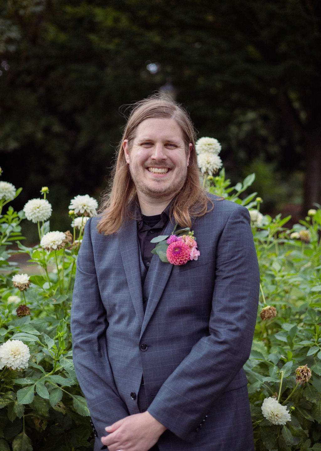 Groom in a grey checked suit and dahlia boutonniere standing in the dahlia garden at Cathedral Park