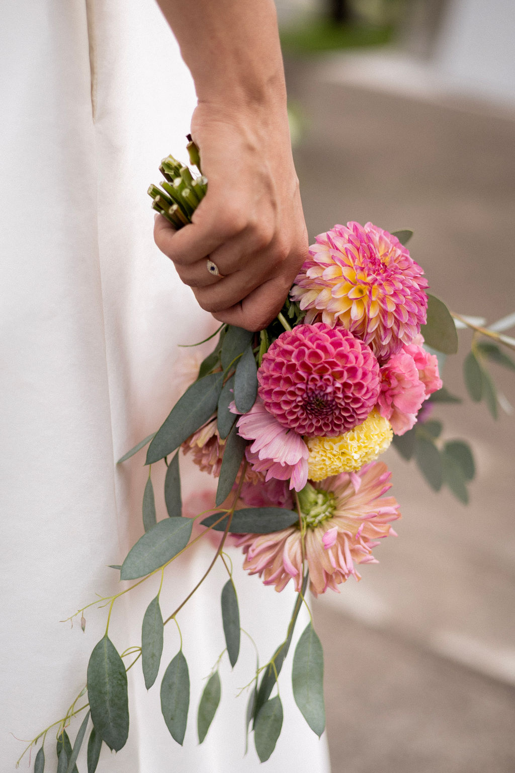 Close up of a Still City Flowers bouquet of dahlias and eucalyptus held against a satin wedding dress