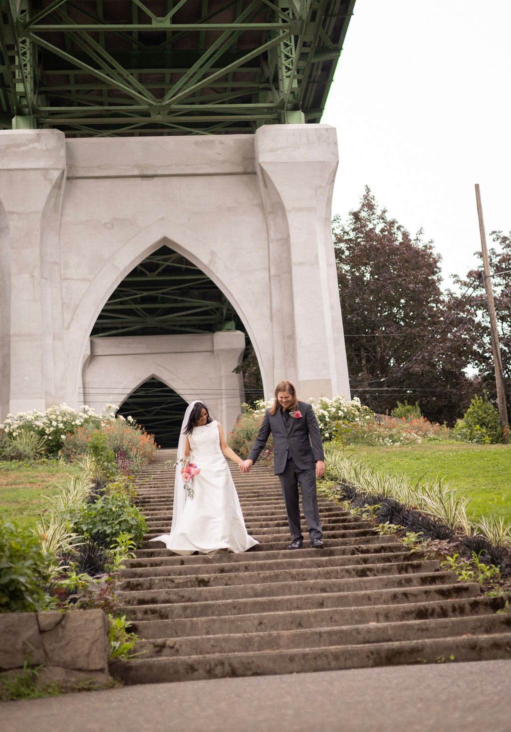 A couple walking down the Cathedral Park staircase under the St. Johns Bridge arch after their ceremony