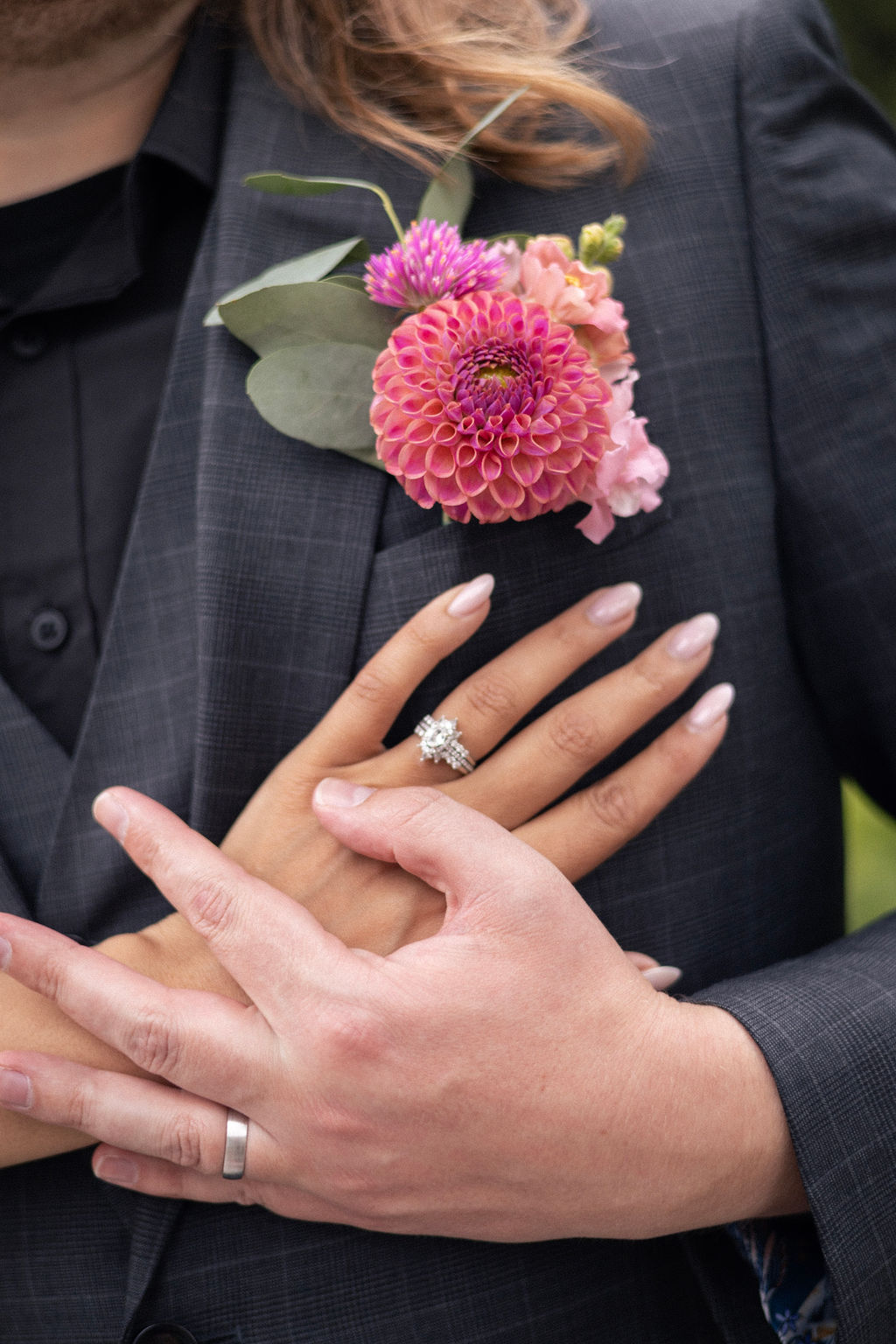 Close up of the couple's hands and wedding rings resting against a dahlia boutonniere