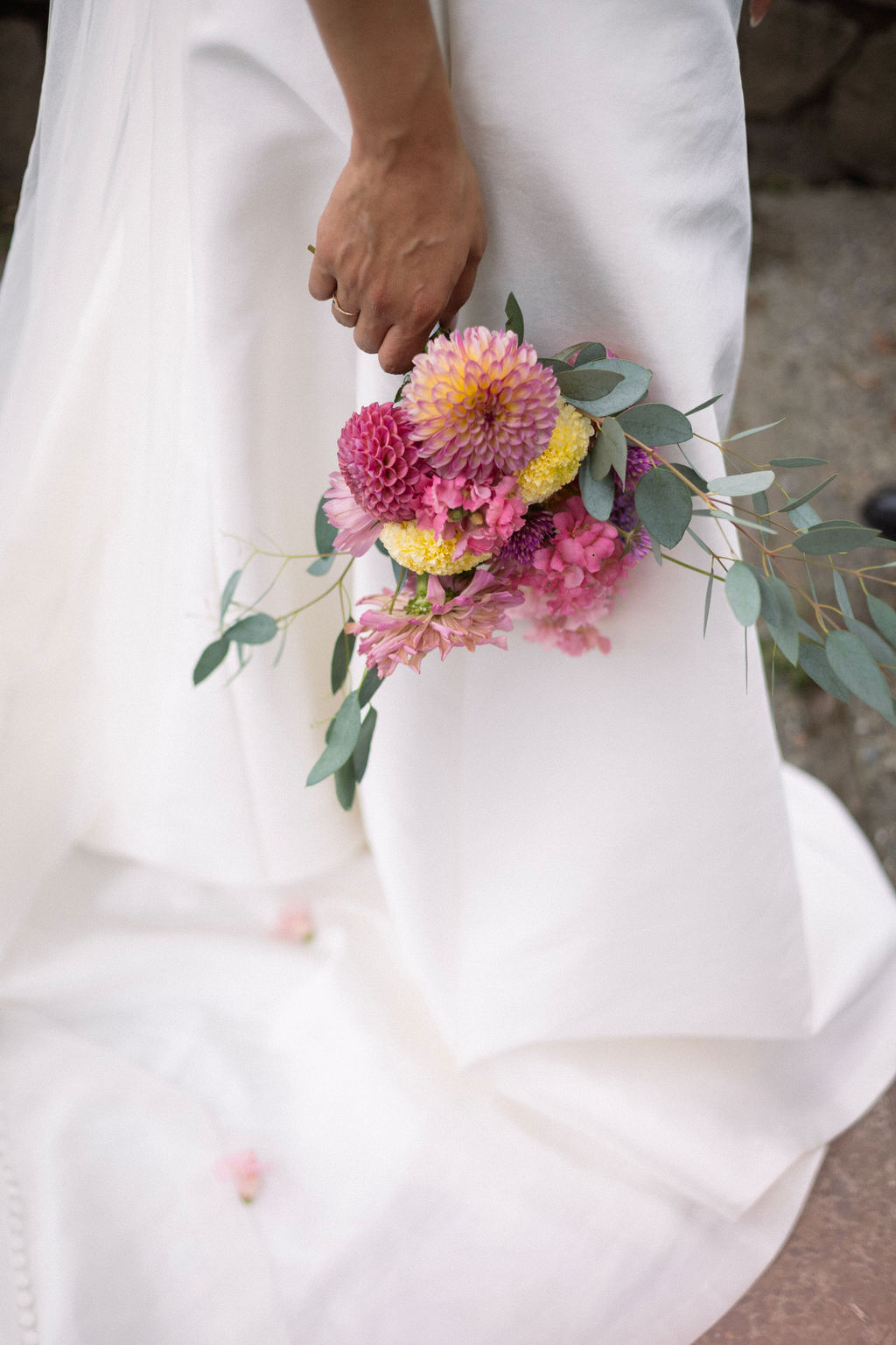 A bride holding her dahlia bouquet at her side with the train of her dress spread behind her