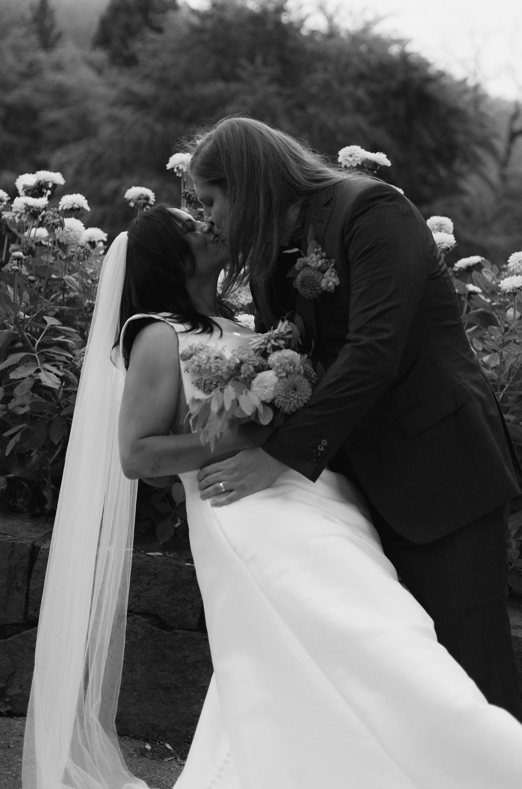 Black and white photograph of newlyweds kissing among the dahlias at Cathedral Park